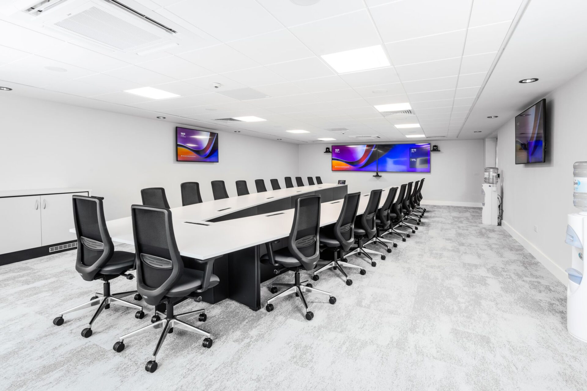 arge white boardroom table with integrated cable access, black mesh chairs and wall-mounted screens in a modern meeting room.