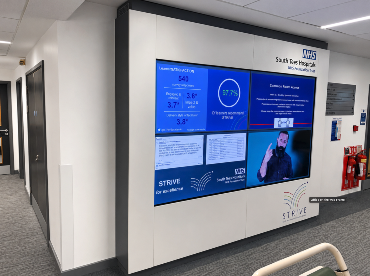 Four-screen video wall set within white fitted panelling with South Tees Hospitals NHS and STRIVE branding.